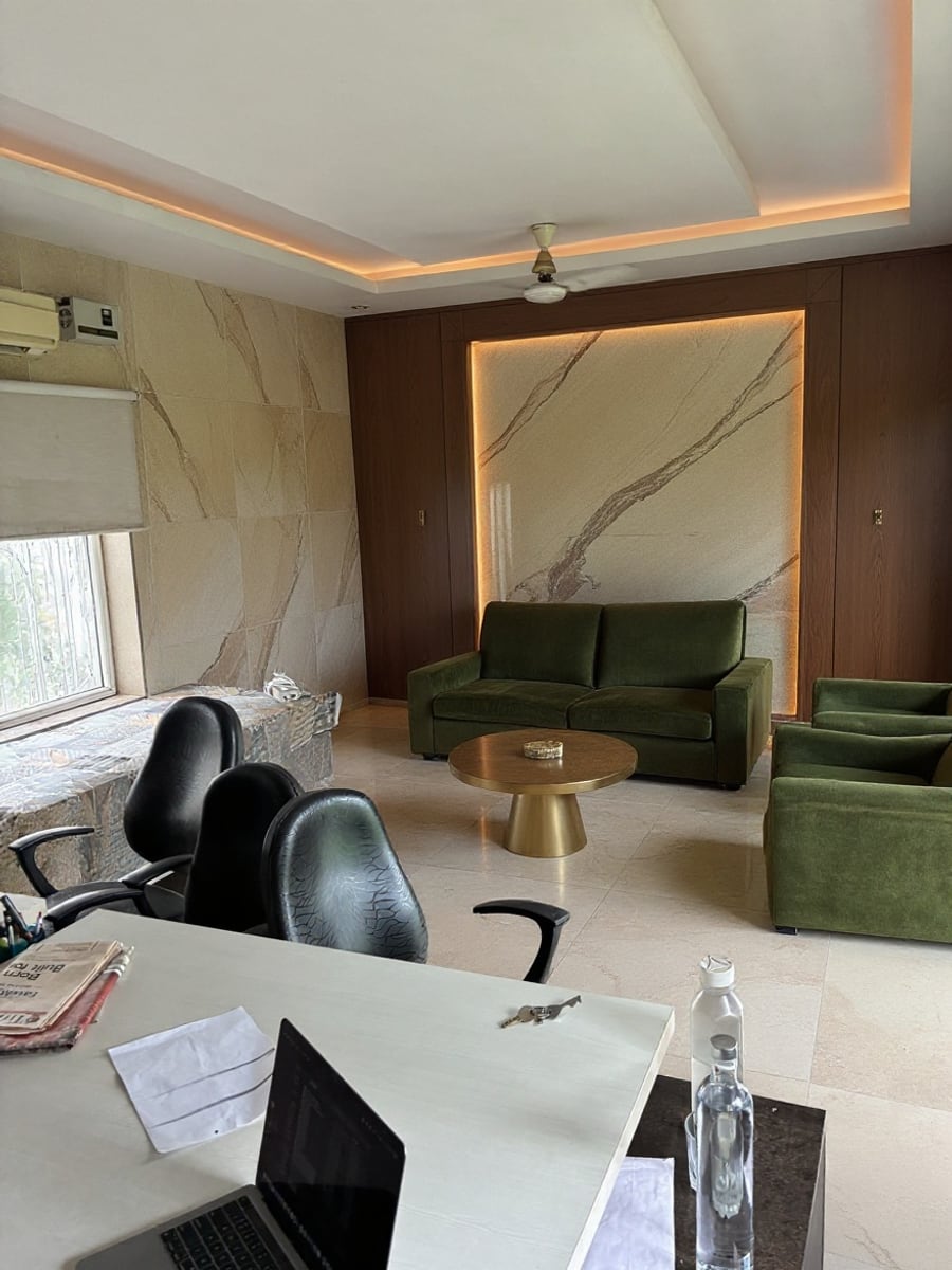After: the same room in stone and walnut panelling with a backlit marble panel and cove lighting — ceiling fan, split AC, window and desk unchanged
