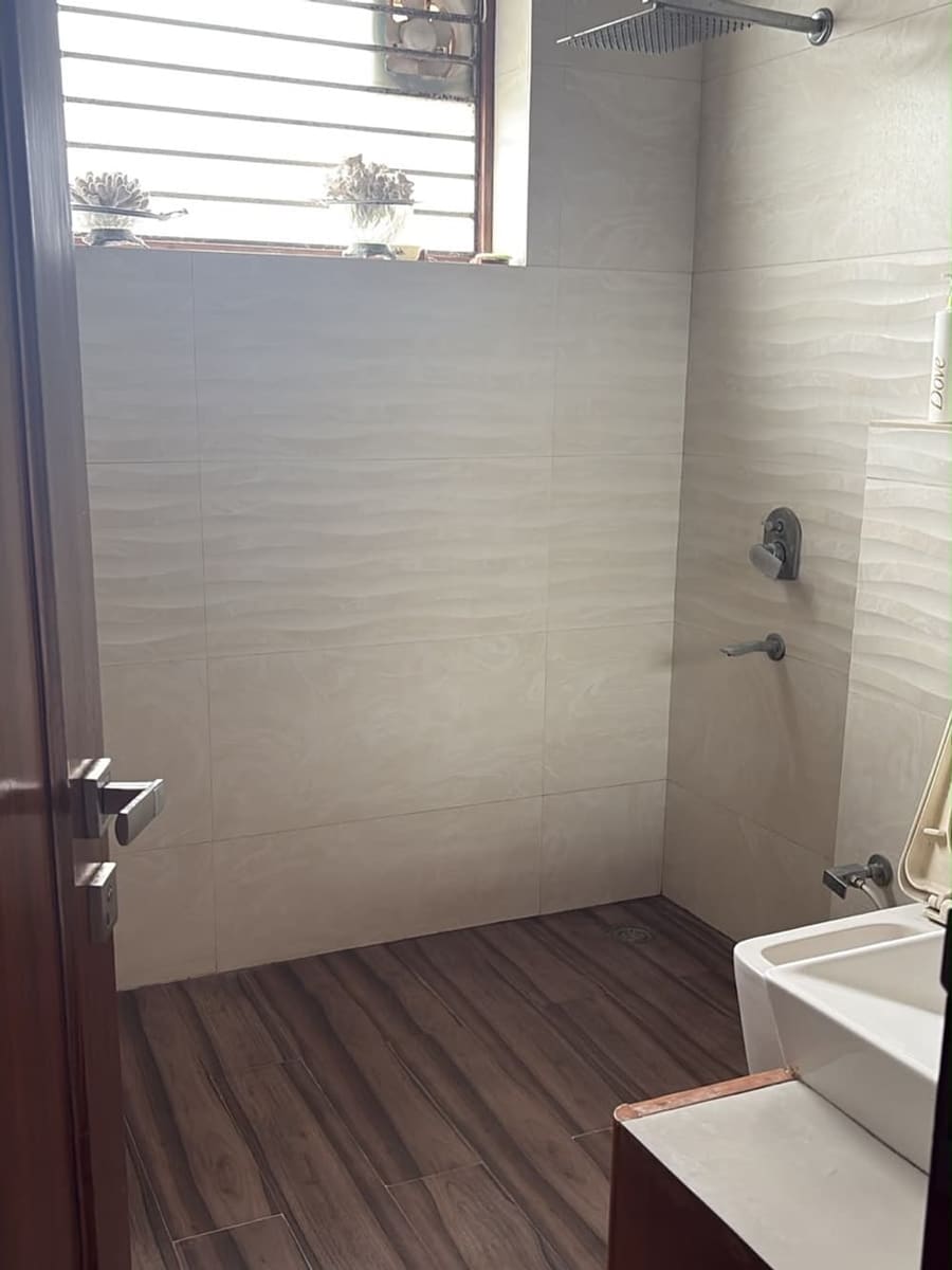 Before: an ordinary Indian bathroom with a barred window, exhaust vent and wood-look floor tile